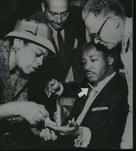 Martin Luther King gets first aid in Harlem store after he was stabbed in 1958. Friends wrap finger, leave weapon sticking in chest. (Removal of weapon might have caused fatal hemorrhage)